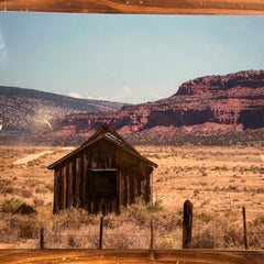 A scenic print of a desert landscape with a wooden cabin and mountains.