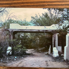 Abandoned structure with overgrown vegetation on a dirt path, framed in wooden border.