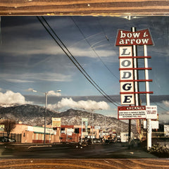 Reflective surface showing a vintage-style 'Bow & Arrow Lodge' sign with mountains in the background.