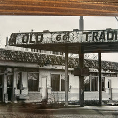 Black and white photo of a building with 'Old 66 Trading' sign on a wooden frame.