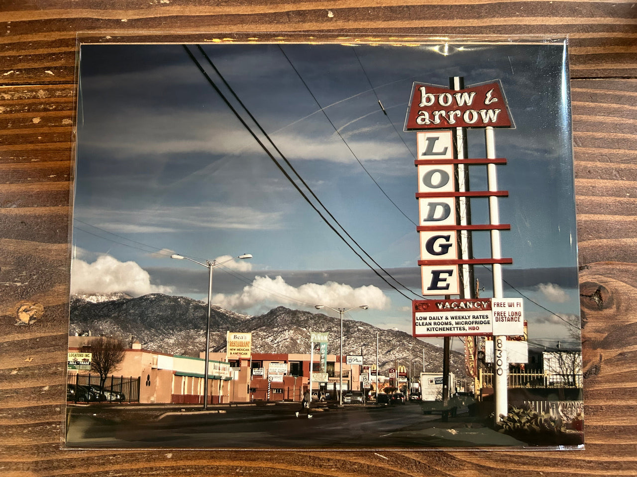 Reflective surface showing a vintage-style 'Bow & Arrow Lodge' sign with mountains in the background.